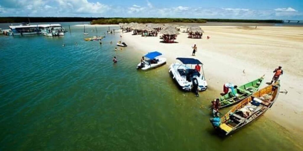 Vista aérea da Crôa do Goré com lanchas, catamarã, barcos, bancos de areia e quiosques sobre águas cristalinas em Aracaju, Sergipe.
