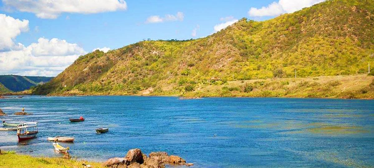 Vista panorâmica do Rio São Francisco em Piranhas, Alagoas, com águas calmas, pequenas embarcações, montanhas ao fundo e paisagem natural do sertão nordestino.