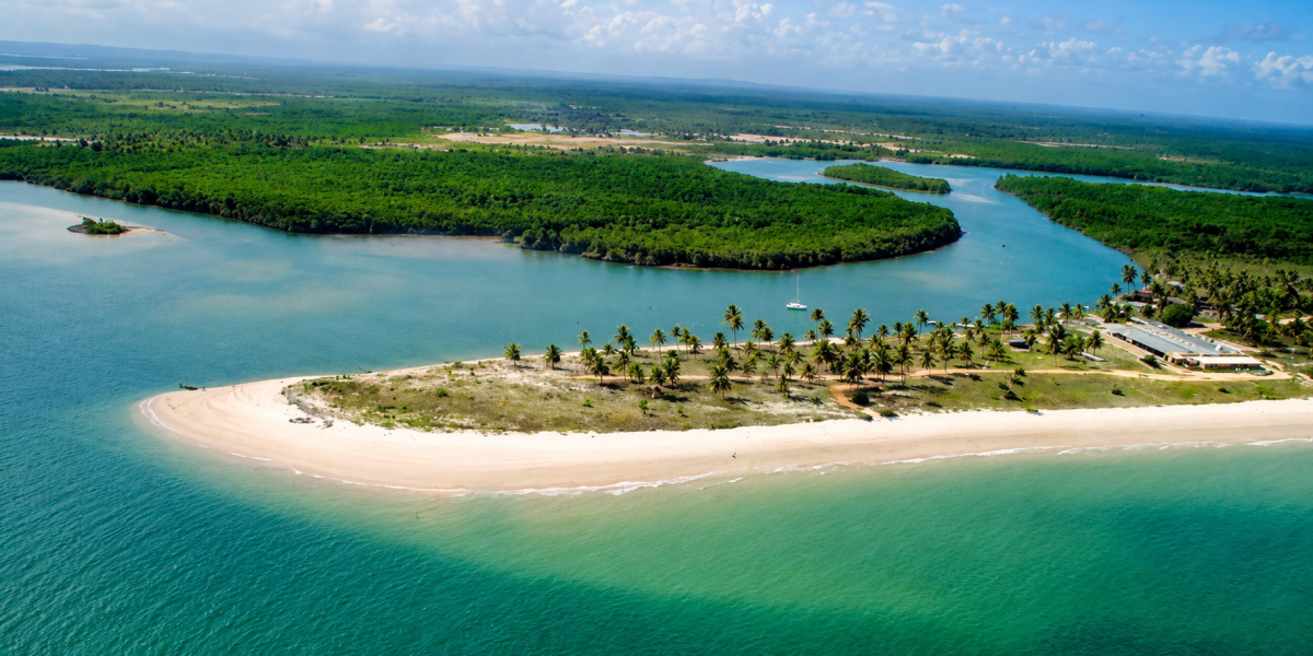 Vista aérea da Foz do Rio Real em Mangue Seco, mostrando praias de areia branca, manguezais preservados, coqueirais e águas cristalinas na divisa entre Sergipe e Bahia.