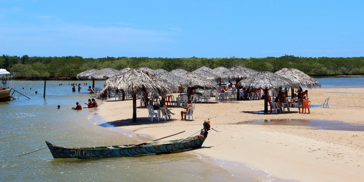 Vista da Ilha Croa do Goré, em Aracaju, Sergipe, com bancos de areia, quiosques de palha, canoa tradicional, águas calmas e visitantes durante o passeio de catamarã.