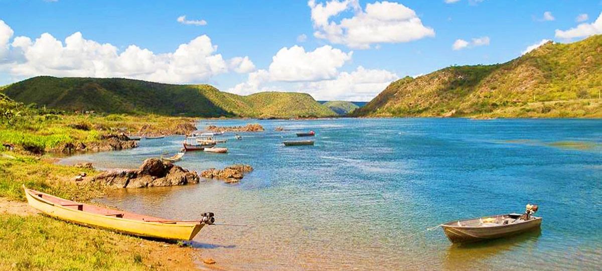 Vista do Rio São Francisco durante a Trilha do Cangaço em Piranhas, Alagoas, com barcos e paisagem natural.